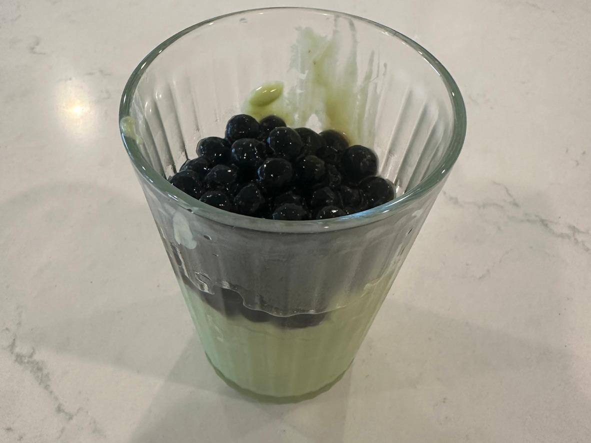 Pale green avocado banana milk topped with black tapioca pearls in a clear glass