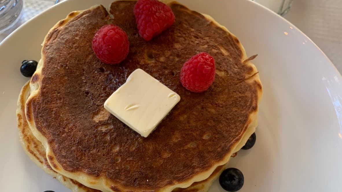 Stack of buttermilk pancakes with butter, raspberries, blueberries, and maple syrup