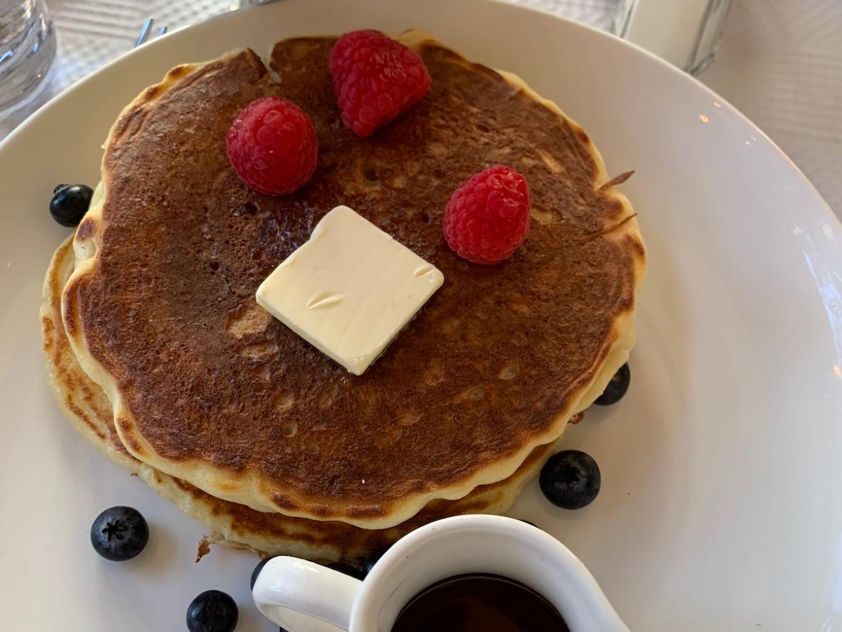 Stack of buttermilk pancakes with butter, raspberries, blueberries, and maple syrup
