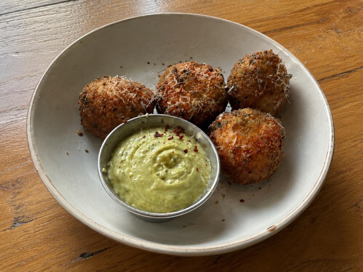 Four cacio e pepe arancini around a bowl of green pesto mayonnaise