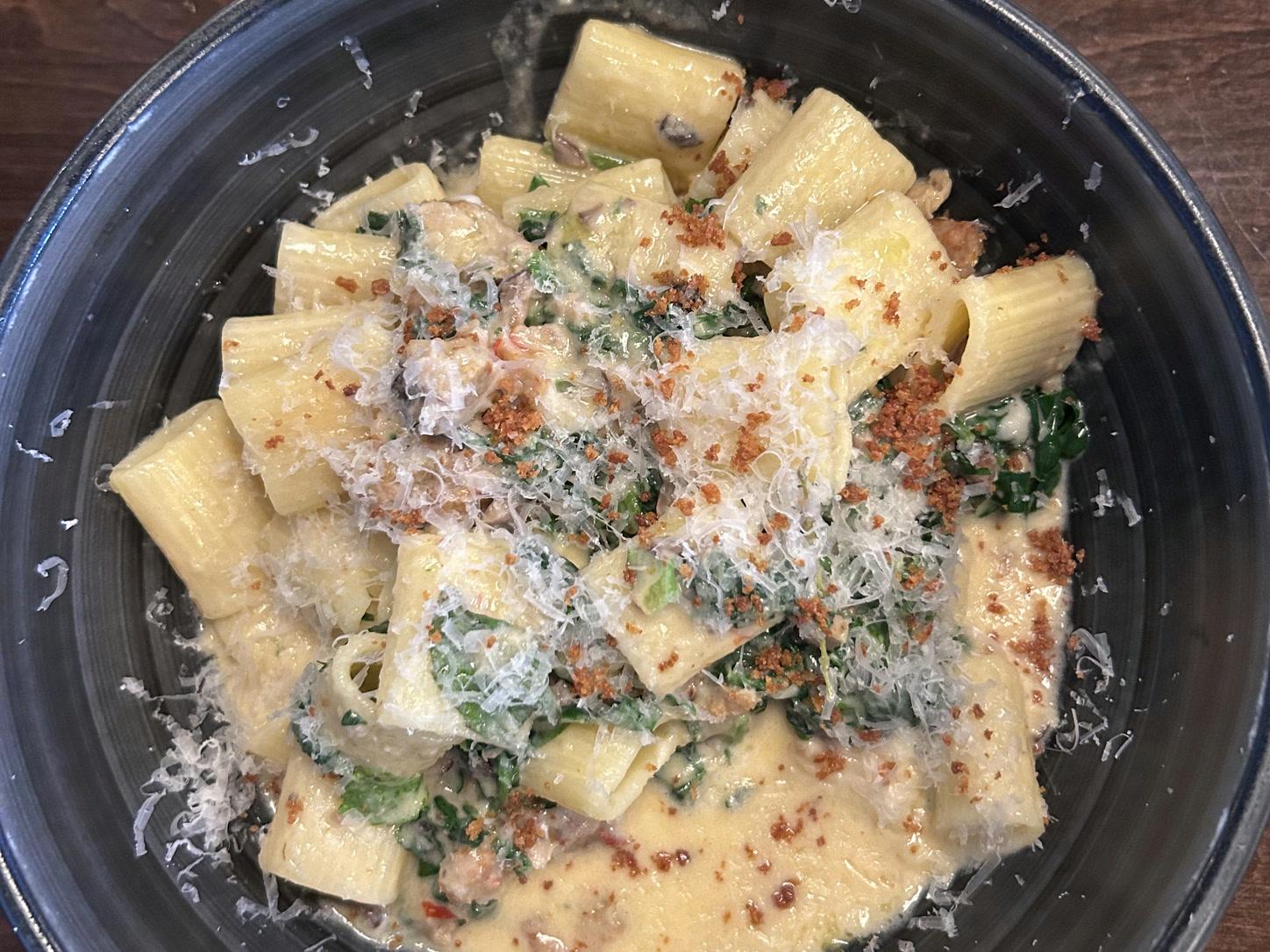 Creamy Calabrian rigatoni with chicken sausage, roasted mushrooms, spinach, and pecorino breadcrumbs in a black bowl