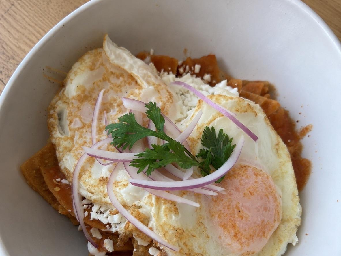 Chilaquiles rojos topped with fried eggs, red onion, cilantro, and crema