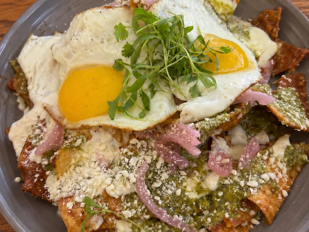 Chilaquiles verdes topped with two fried eggs, crema, red onion, and herbs