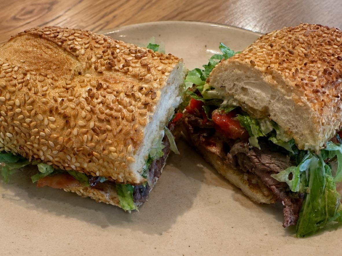 Chimichurri steak and bacon sandwich on a sesame roll with greens