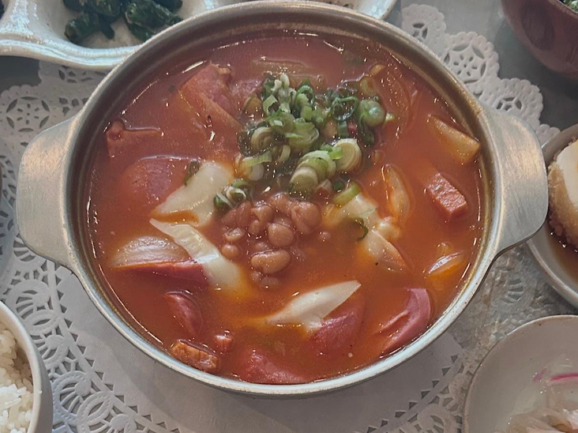 Korean army soup with tofu, sausage, noodles, kimchi, and scallions in red broth