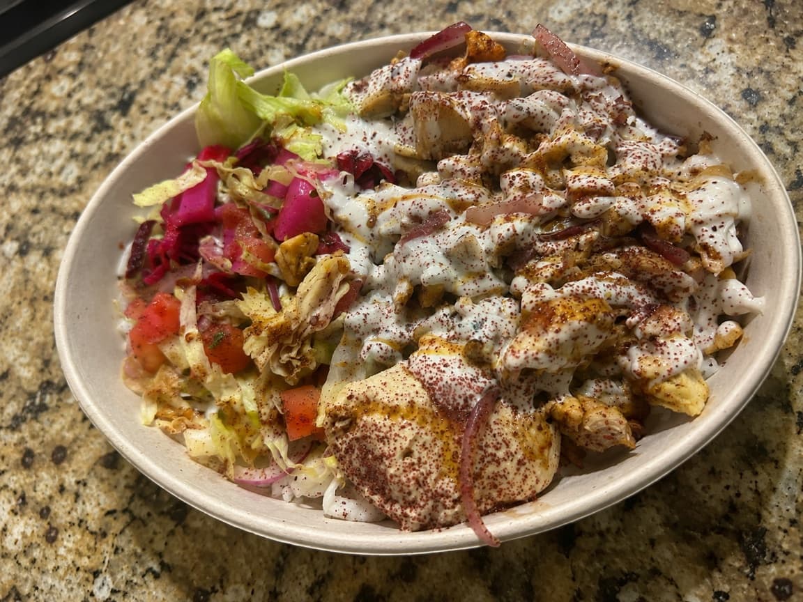 Homemade Egyptian chicken shawarma bowl with basmati rice, hummus, Jerusalem salad, pickles, red cabbage, lettuce, and white sauce