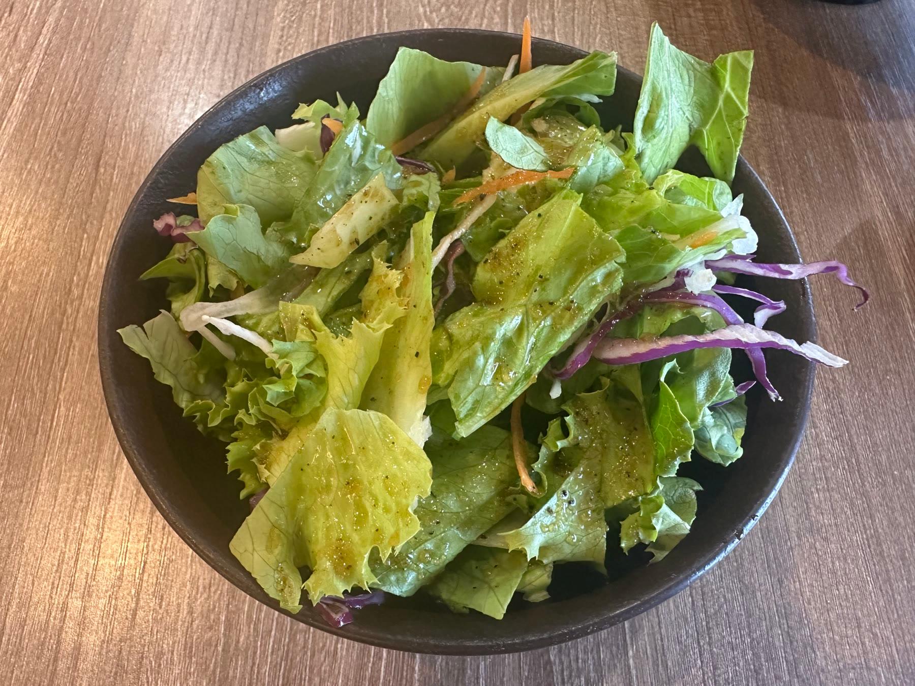 Japanese green salad with mixed lettuce, red cabbage, shredded carrot, and carrot-ginger dressing in a black bowl