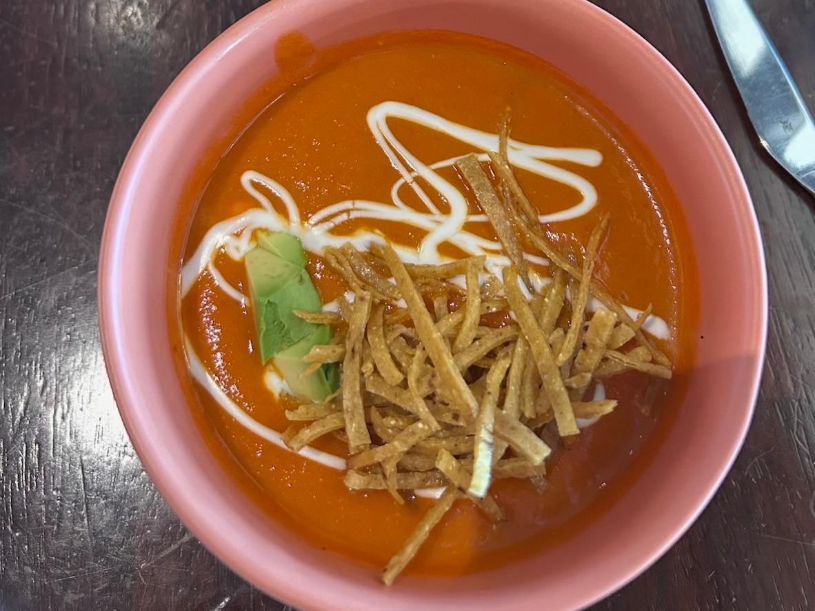 Red tortilla soup topped with crisp tortilla strips, crema, and cilantro