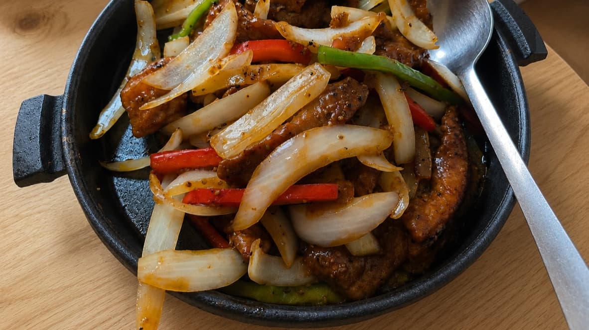 Sizzling black pepper beef with onions and bell peppers on a cast-iron plate