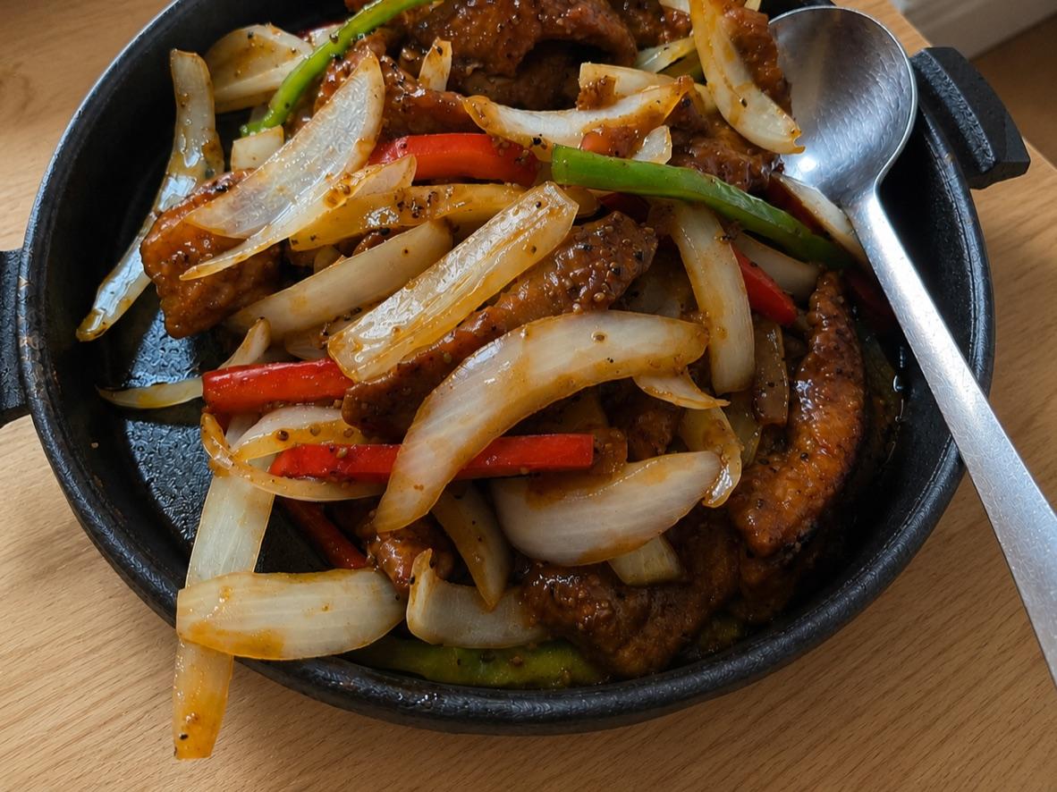 Sizzling black pepper beef with onions and bell peppers on a cast-iron plate