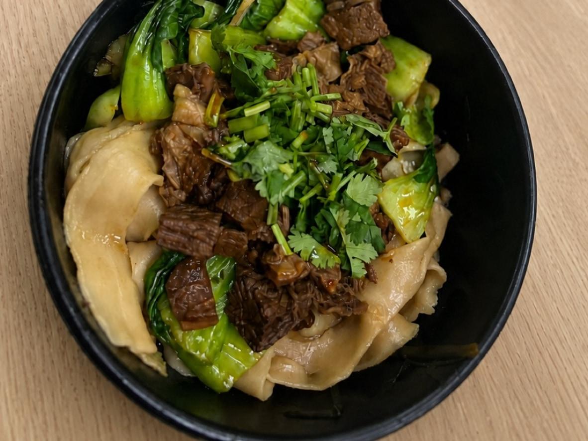 Wide noodles with braised beef, bok choy, cilantro, and peppers in a black bowl