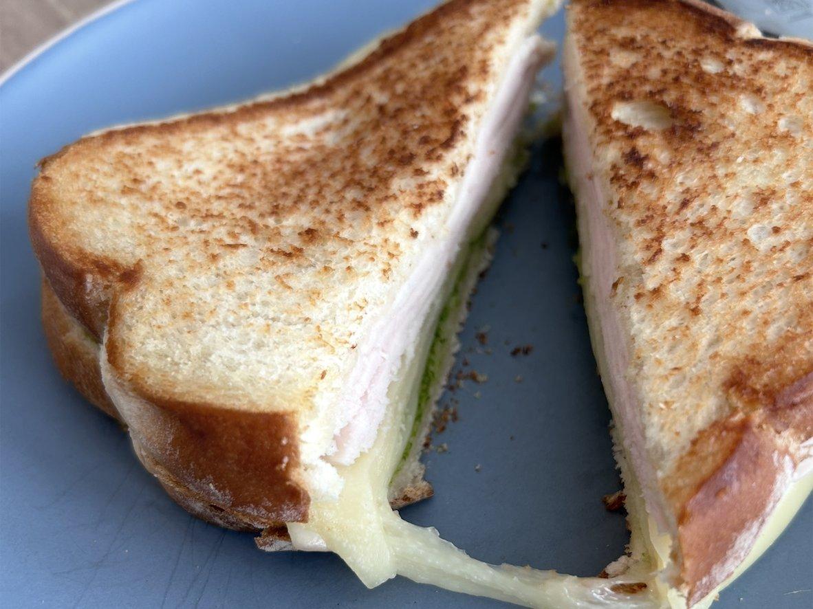 Toasted turkey, pesto, and melted Gouda sandwich cut open on a plate