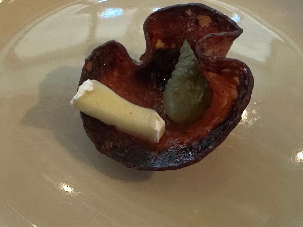 Crisp baked salami cup filled with Brie and a cornichon on a floral plate