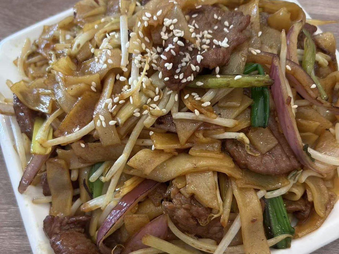 Beef chow fun with wide rice noodles, bean sprouts, scallions, and sesame seeds