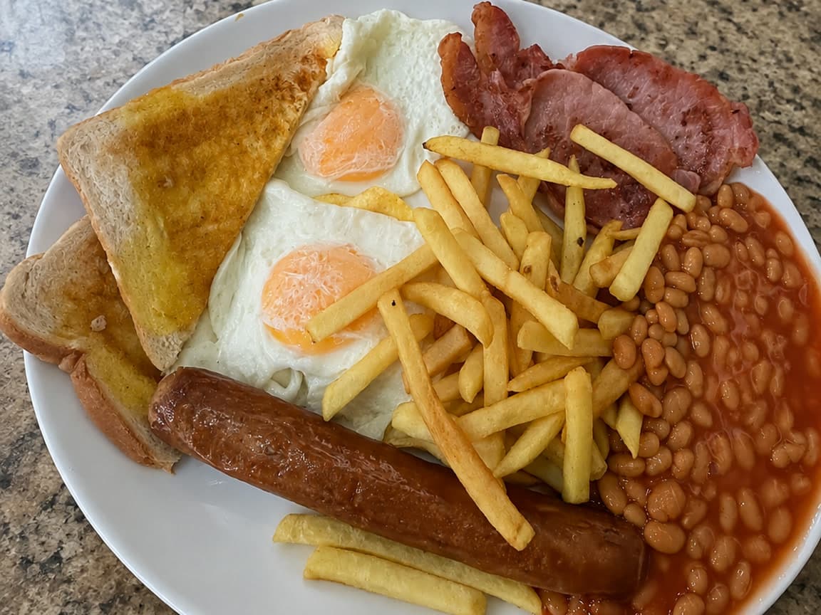 British café breakfast with fried eggs, pork sausage, bacon, baked beans, buttered toast and chips