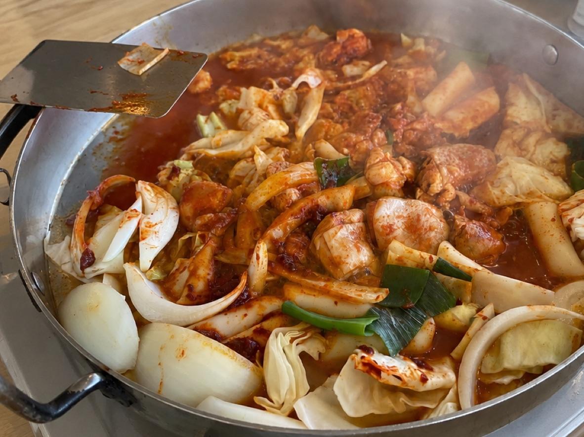 Dak-galbi with spicy chicken, cabbage, rice cakes, and onions cooking in a skillet