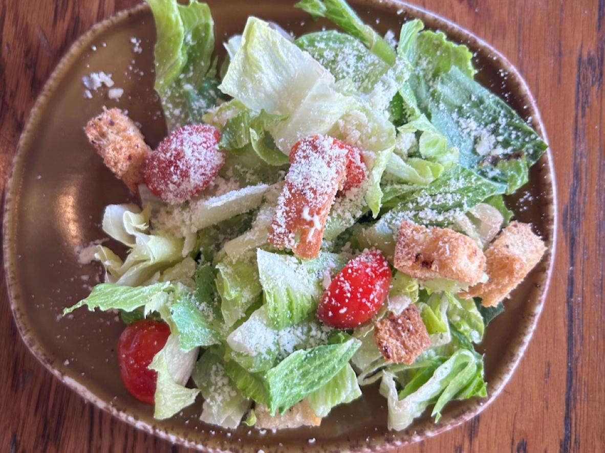 Caesar side salad with romaine, grape tomatoes, grated Parmesan, and garlic croutons on a brown plate