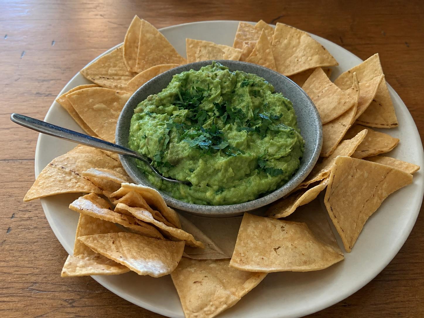 Chunky guacamole topped with cilantro and surrounded by warm tortilla chips on an off-white ceramic platter