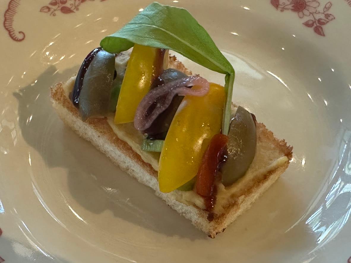 Open-faced hummus toast topped with tomatoes, olives, pickled onion and basil