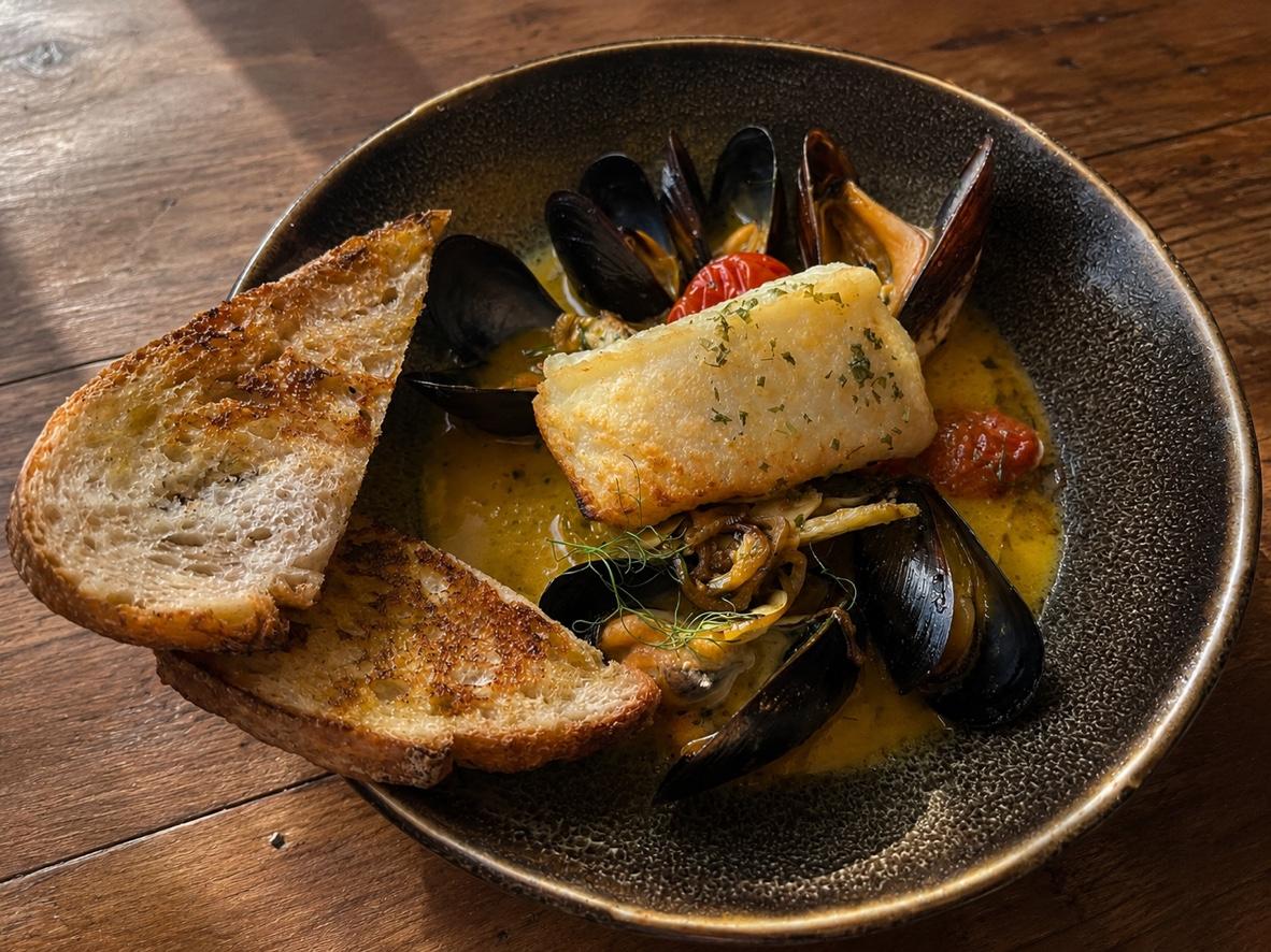 Pan-seared cod with mussels and cherry tomatoes in a golden tomato-fennel broth with toasted sourdough.