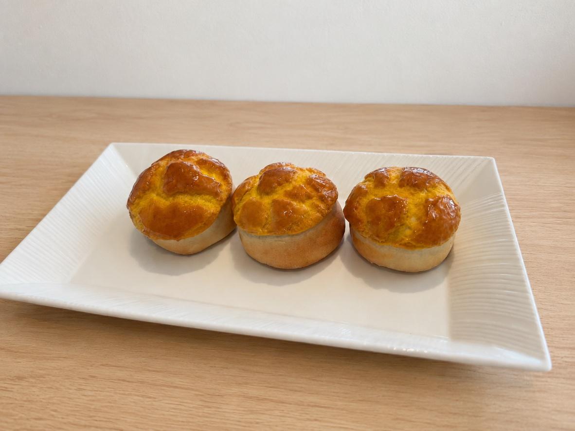 Three pineapple char siu bao with glossy crackled golden tops on a white platter