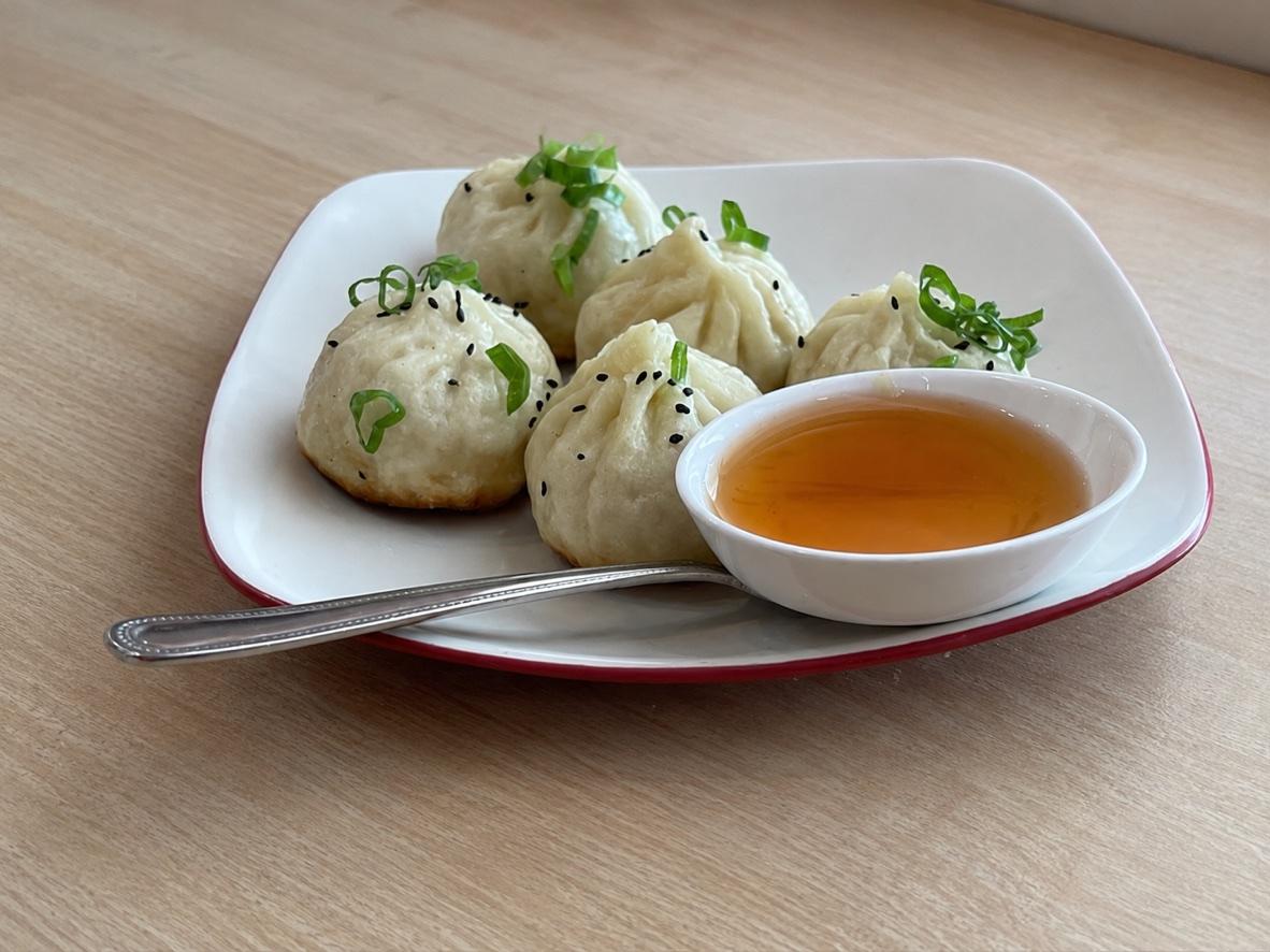 Homemade sheng jian bao topped with scallions and sesame seeds beside a bowl of vinegar